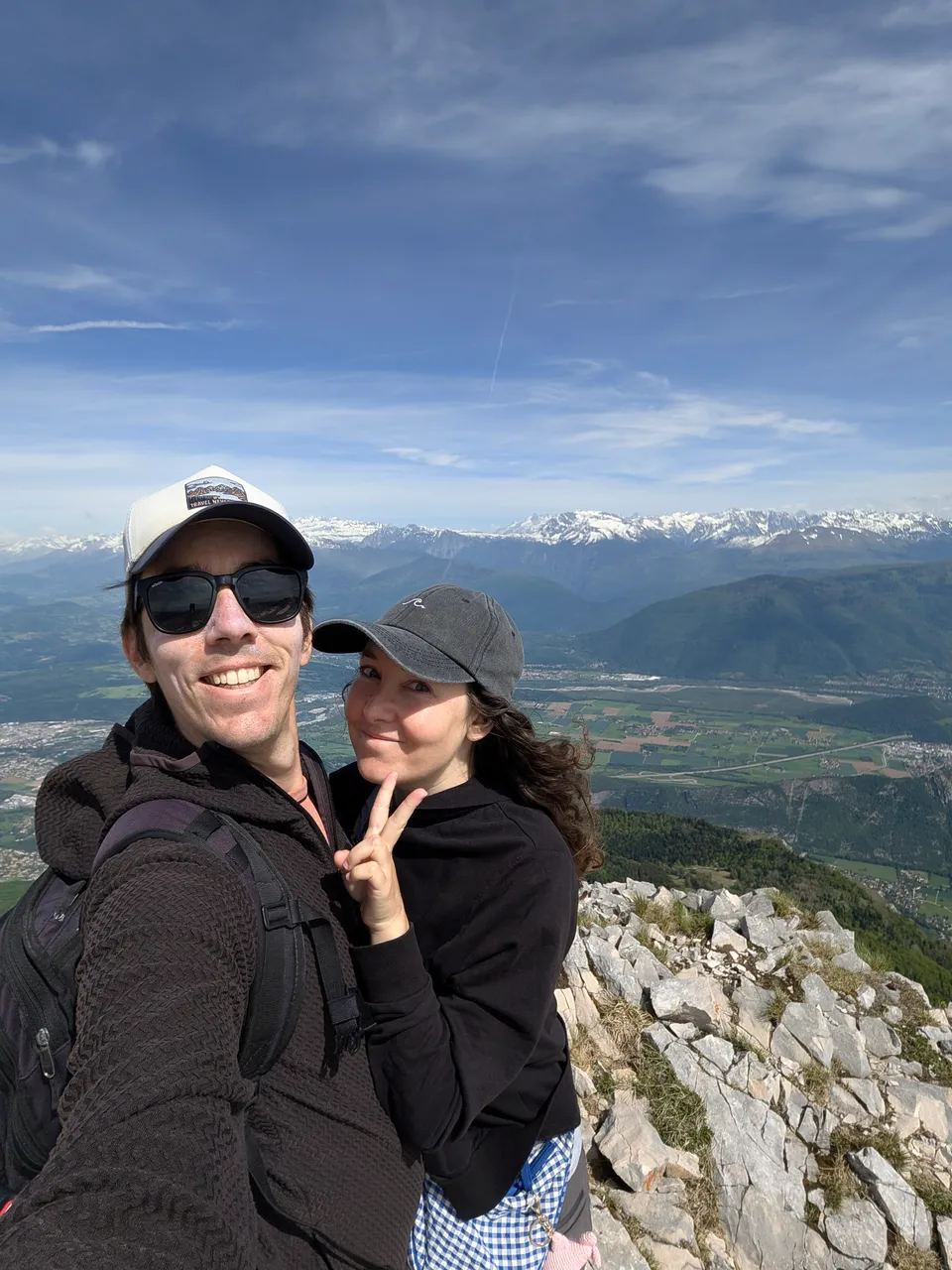 Lola and Yann smiling on a mountain summit above an Alpine valley